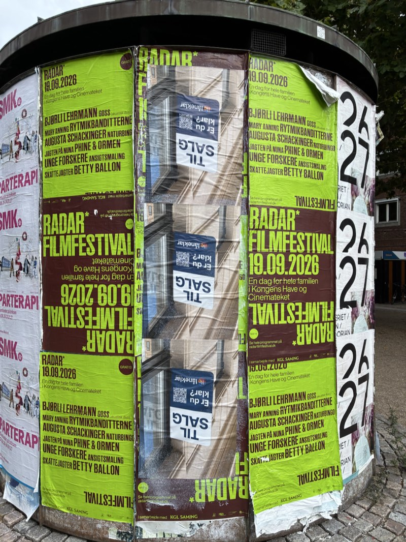 Låneklars plakater mellem festivalplakater på en søjle