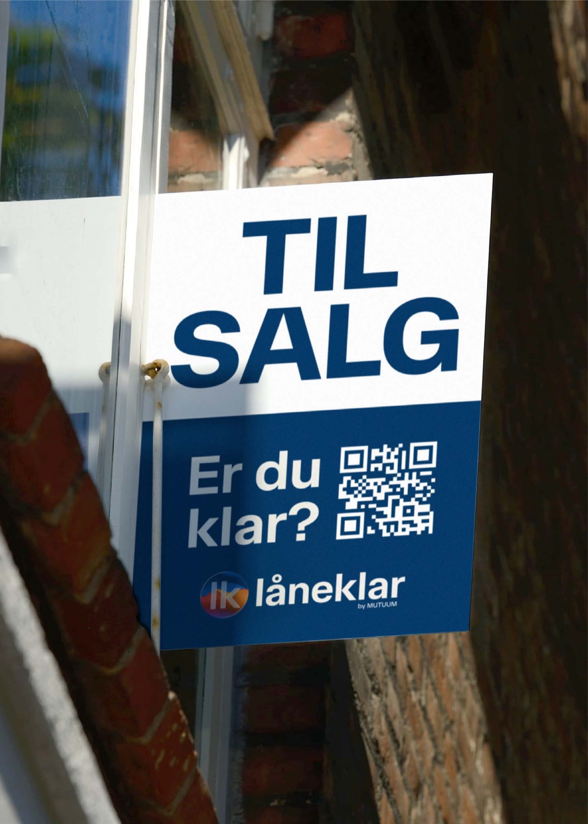 Låneklars skilt med teksten Til salg. Er du klar? hænger i et vindue på en murstensfacade
